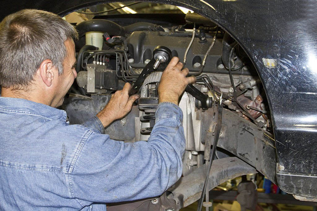 A mechanic, wearing a grease-stained uniform and work gloves, uses a tire iron to carefully remove a damaged tire from a wheel rim.