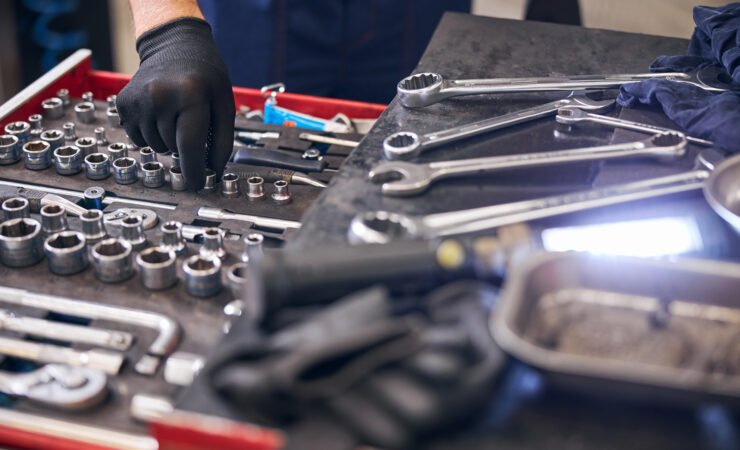 A car mechanic, dressed in a work uniform, reaches into a red toolbox to select a socket wrench for an upcoming repair.