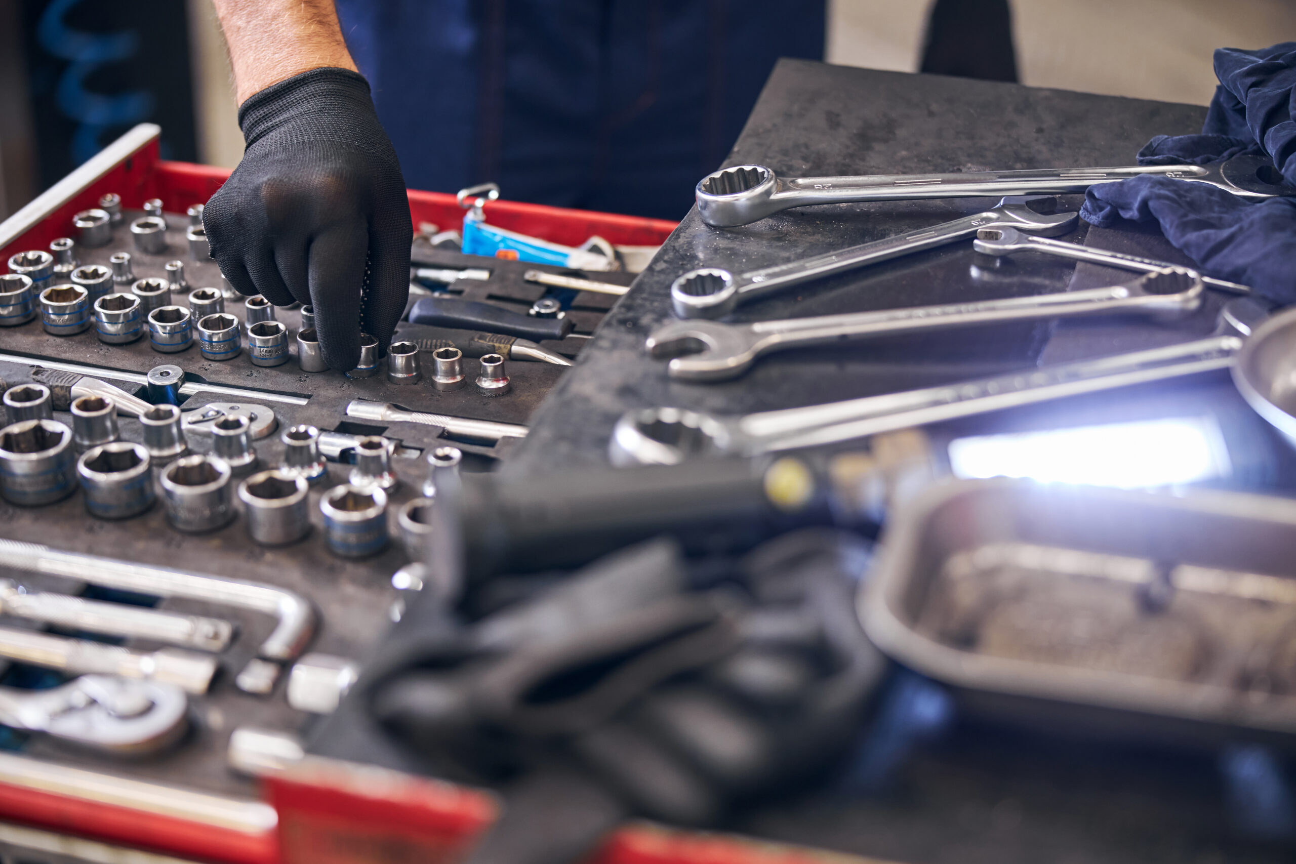 A car mechanic, dressed in a work uniform, reaches into a red toolbox to select a socket wrench for an upcoming repair.