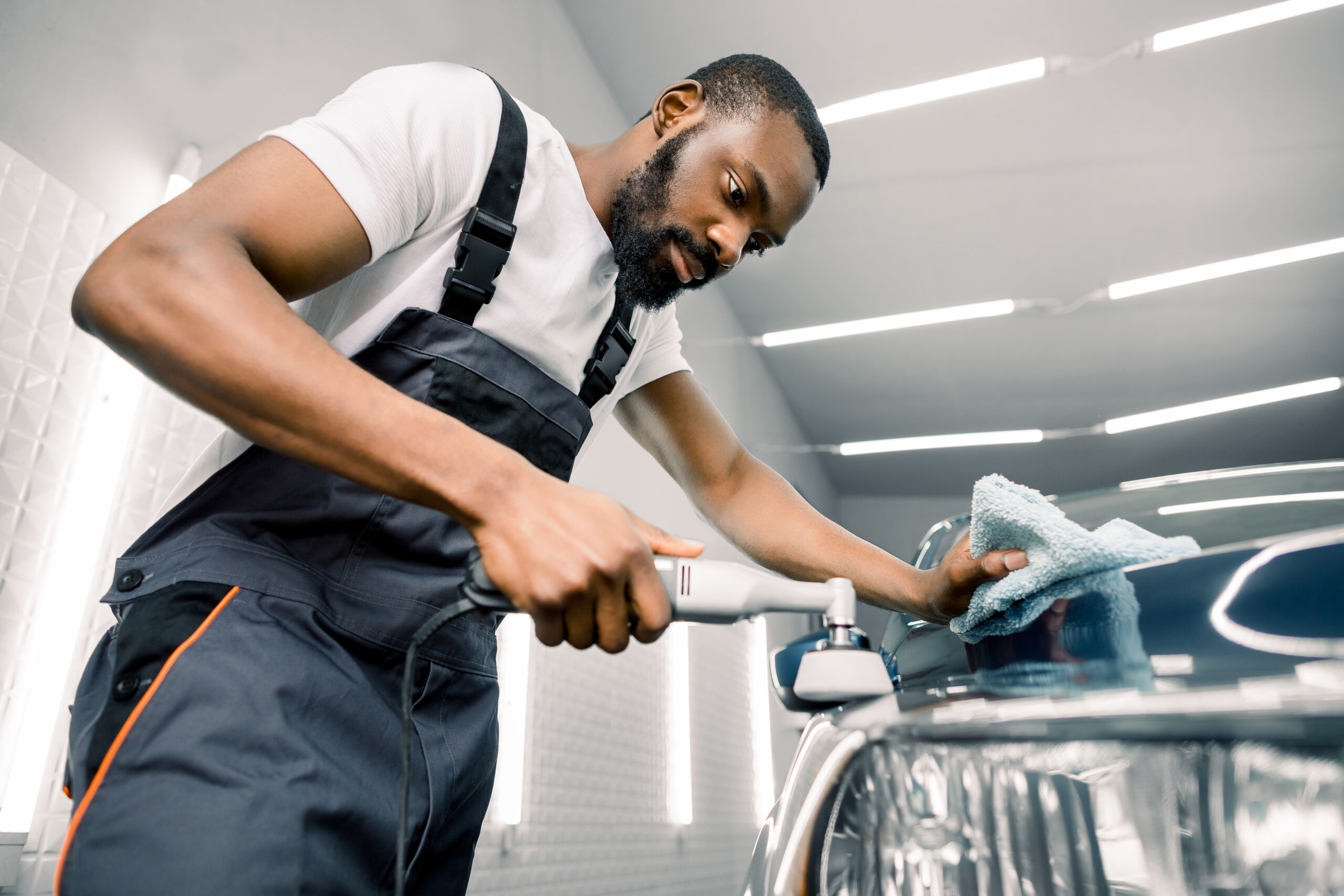 A professional car detailer uses a dual-action polisher and polishing compound to remove swirl marks and imperfections from a car's paint.