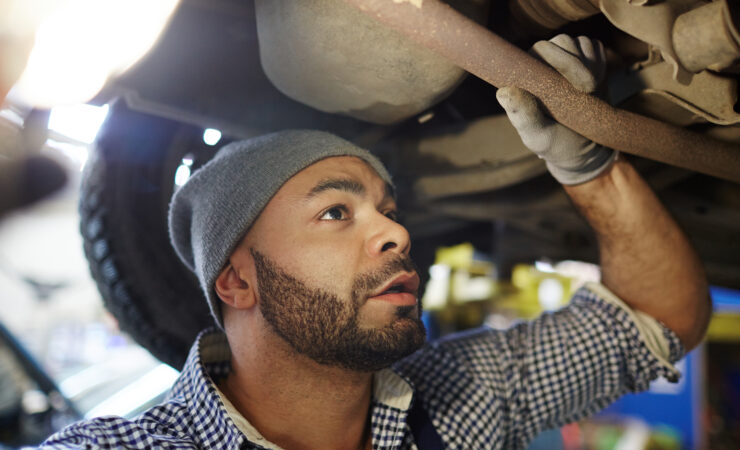 A mechanic in a blue jumpsuit, illuminated by a headlamp, carefully inspects the engine of a car raised on a lift.