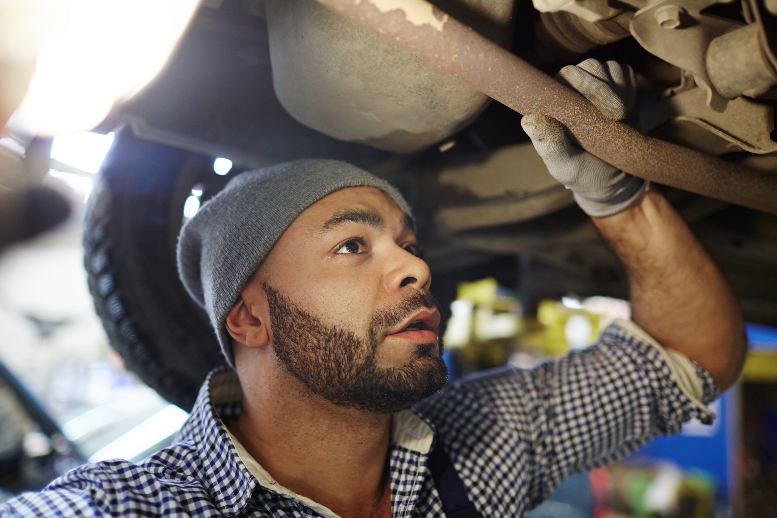 A mechanic in a blue jumpsuit, illuminated by a headlamp, carefully inspects the engine of a car raised on a lift.