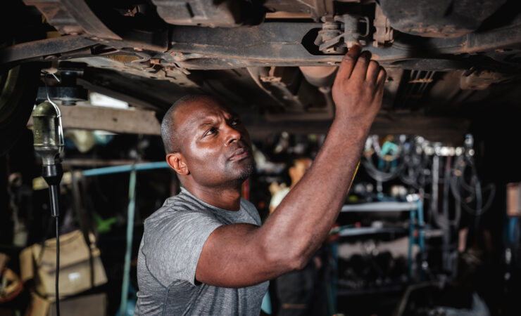 A mechanic in a garage, wearing overalls and holding a wrench, inspects a car.