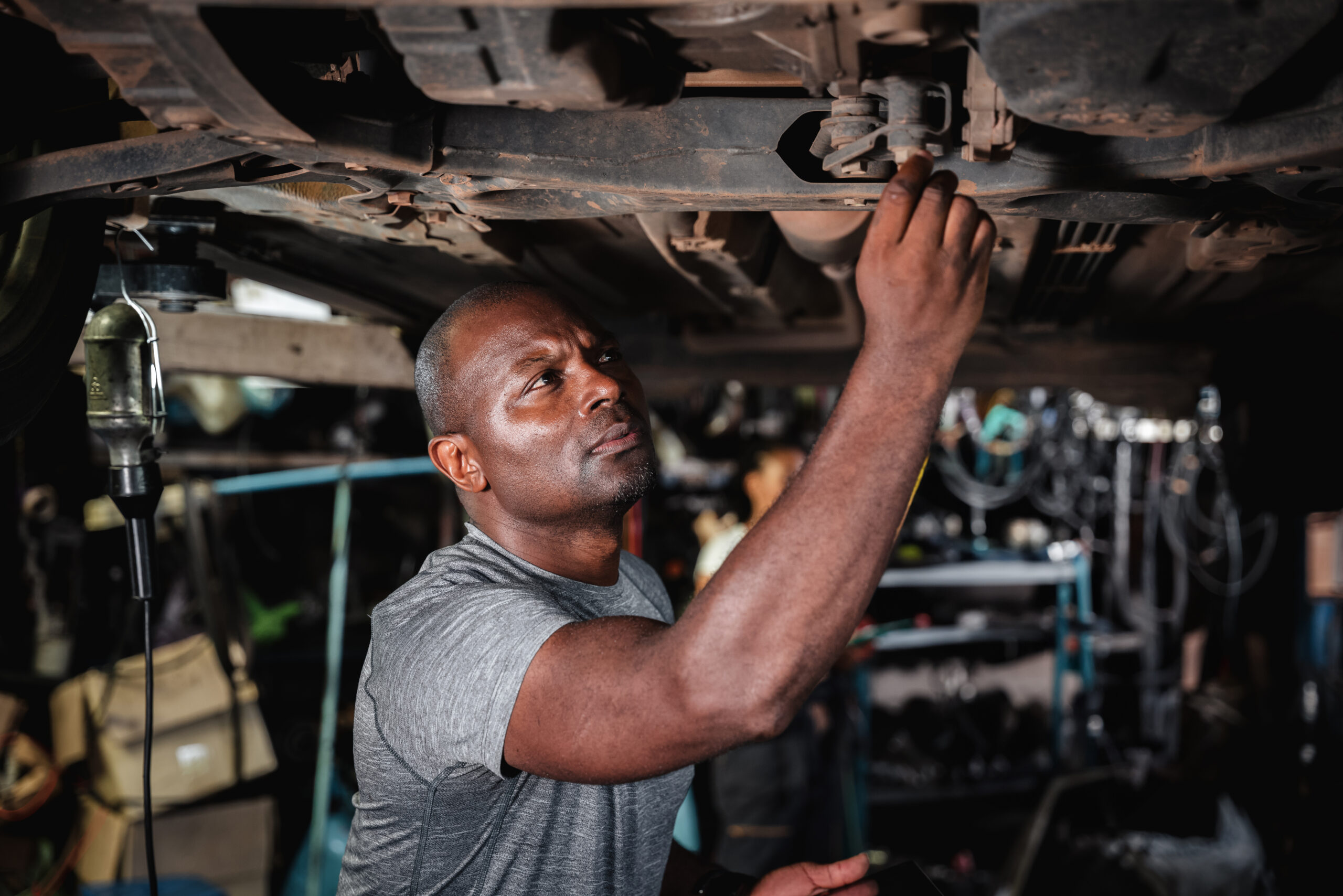 A mechanic in a garage, wearing overalls and holding a wrench, inspects a car.