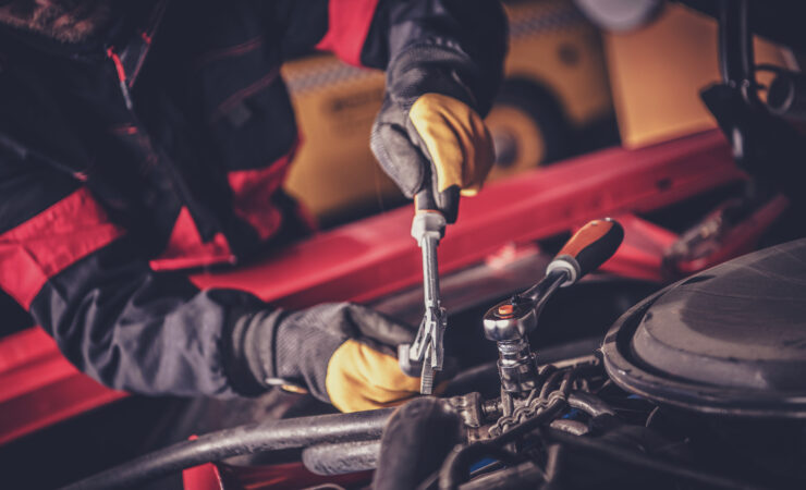 A skilled mechanic leans over the open hood of a classic car, carefully adjusting a carburetor with a screwdriver.