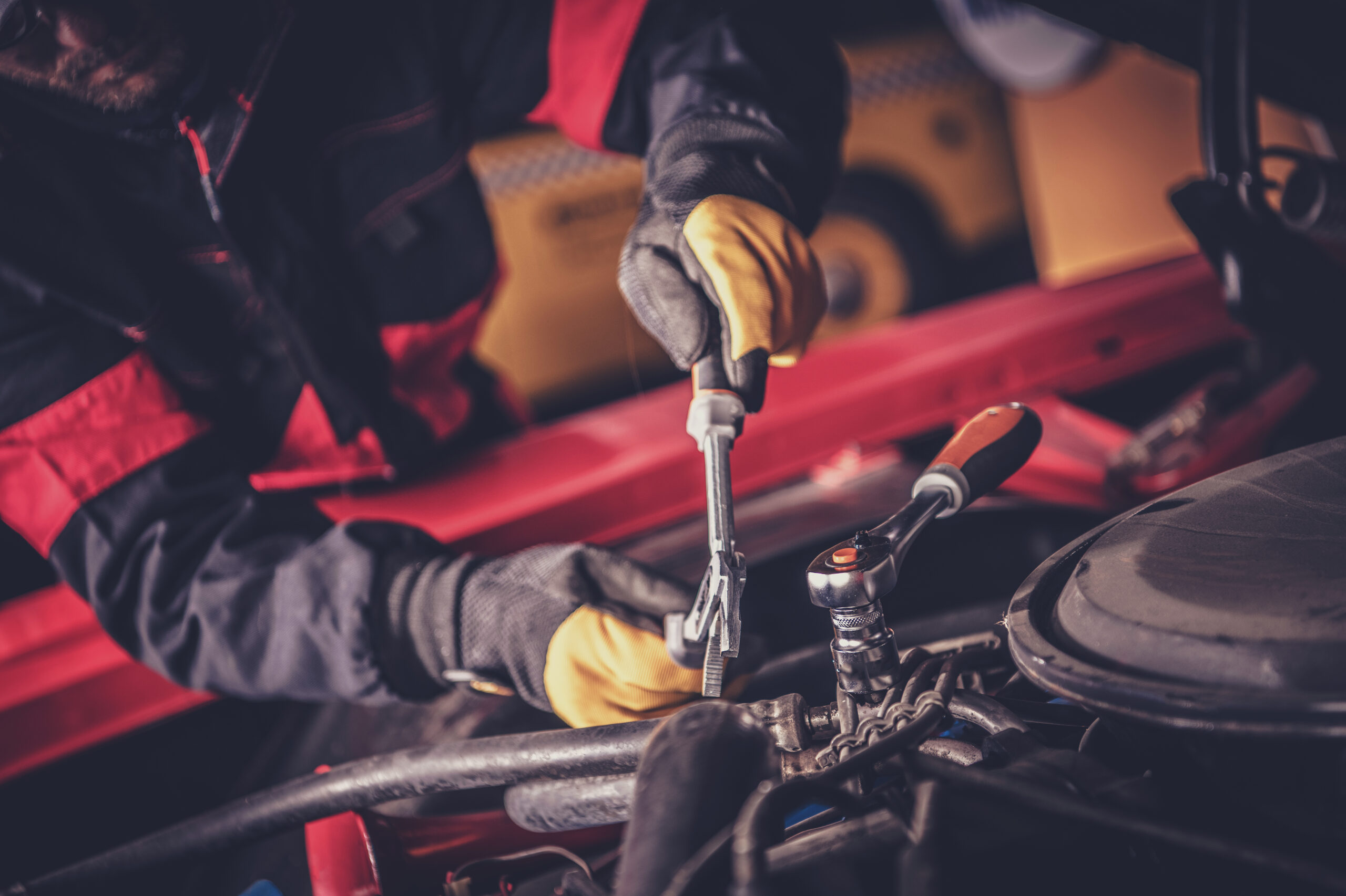 A skilled mechanic leans over the open hood of a classic car, carefully adjusting a carburetor with a screwdriver.