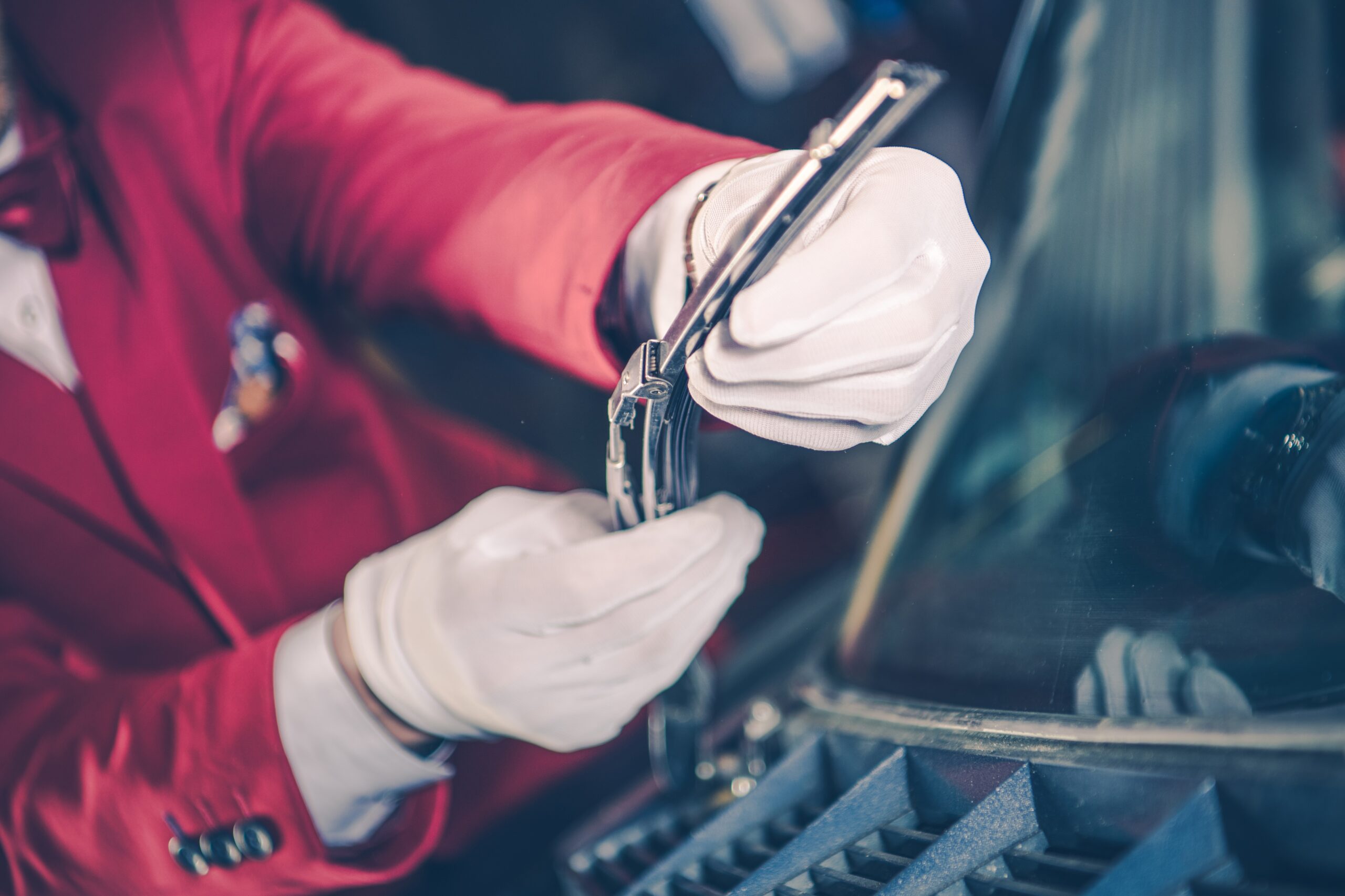 A mechanic's hands, holding a vintage carburetor, carefully install it into the engine bay of a classic car.