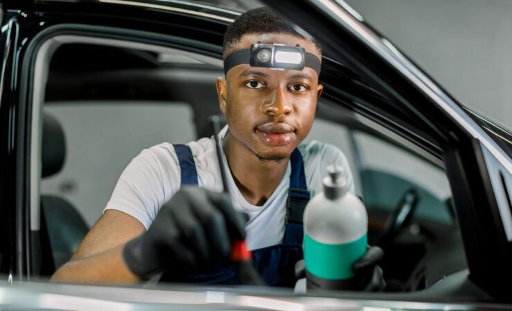 Close-up portrait of a young African man, a car detailing service worker, smiling confidently while holding a polishing pad.