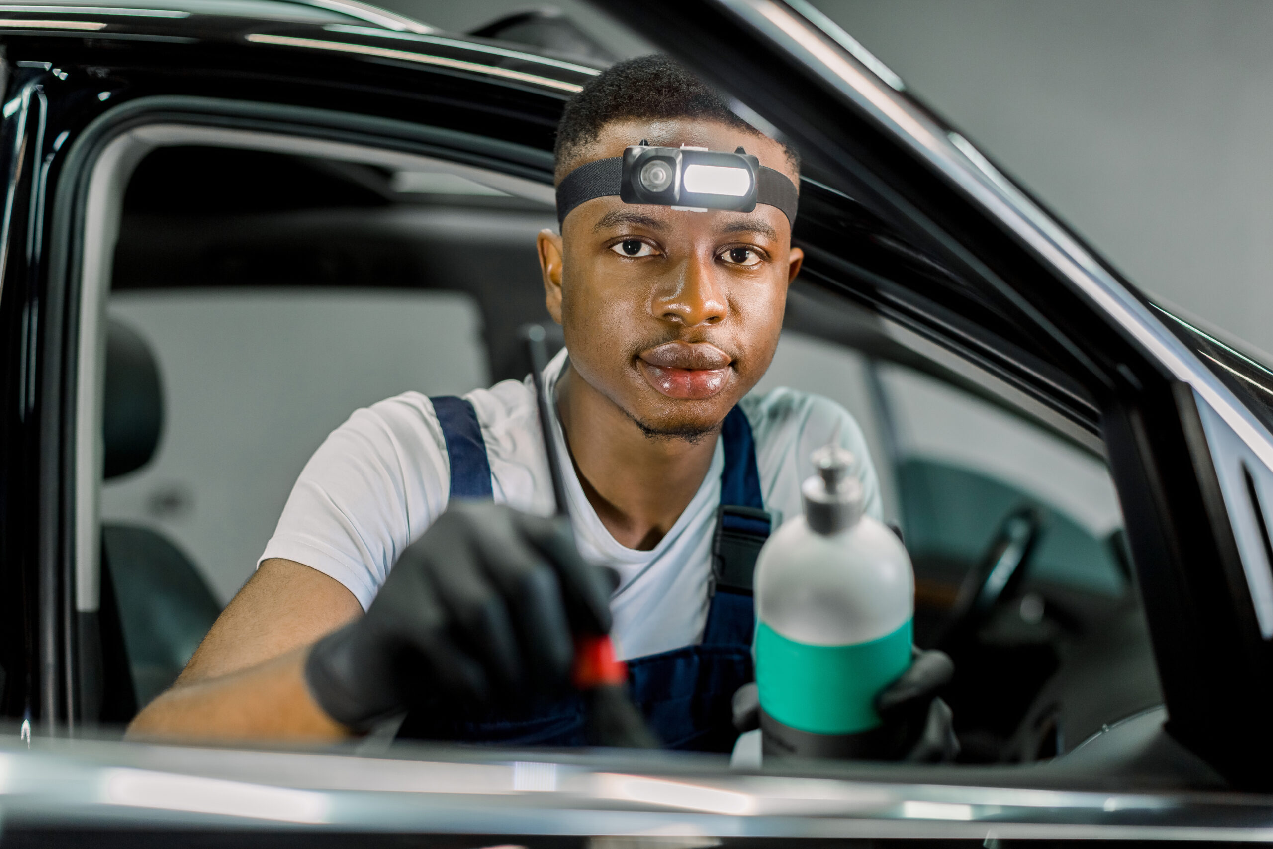 Close-up portrait of a young African man, a car detailing service worker, smiling confidently while holding a polishing pad.