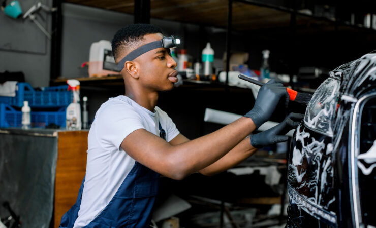 A close-up photo of a young African man wearing protective gloves, his hands holding a specialized tool with a determined expression on his face.