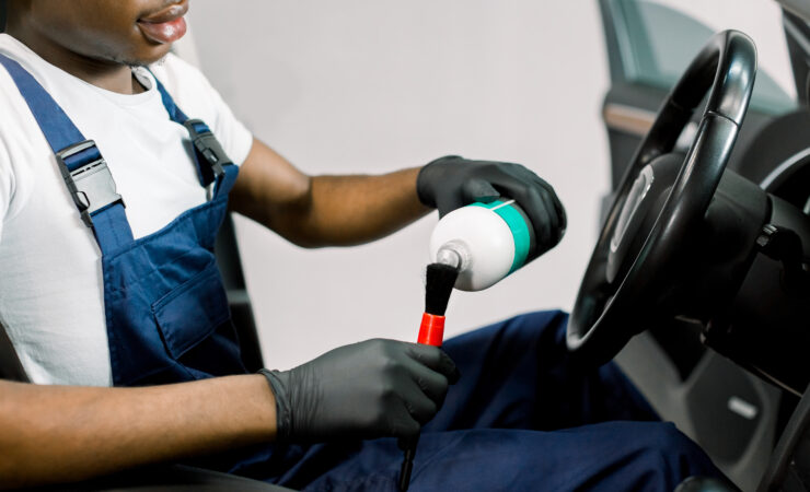 A close-up of a young African man's hands, wearing black nitrile gloves, meticulously applying car wax to a vehicle's exterior with a microfiber cloth.