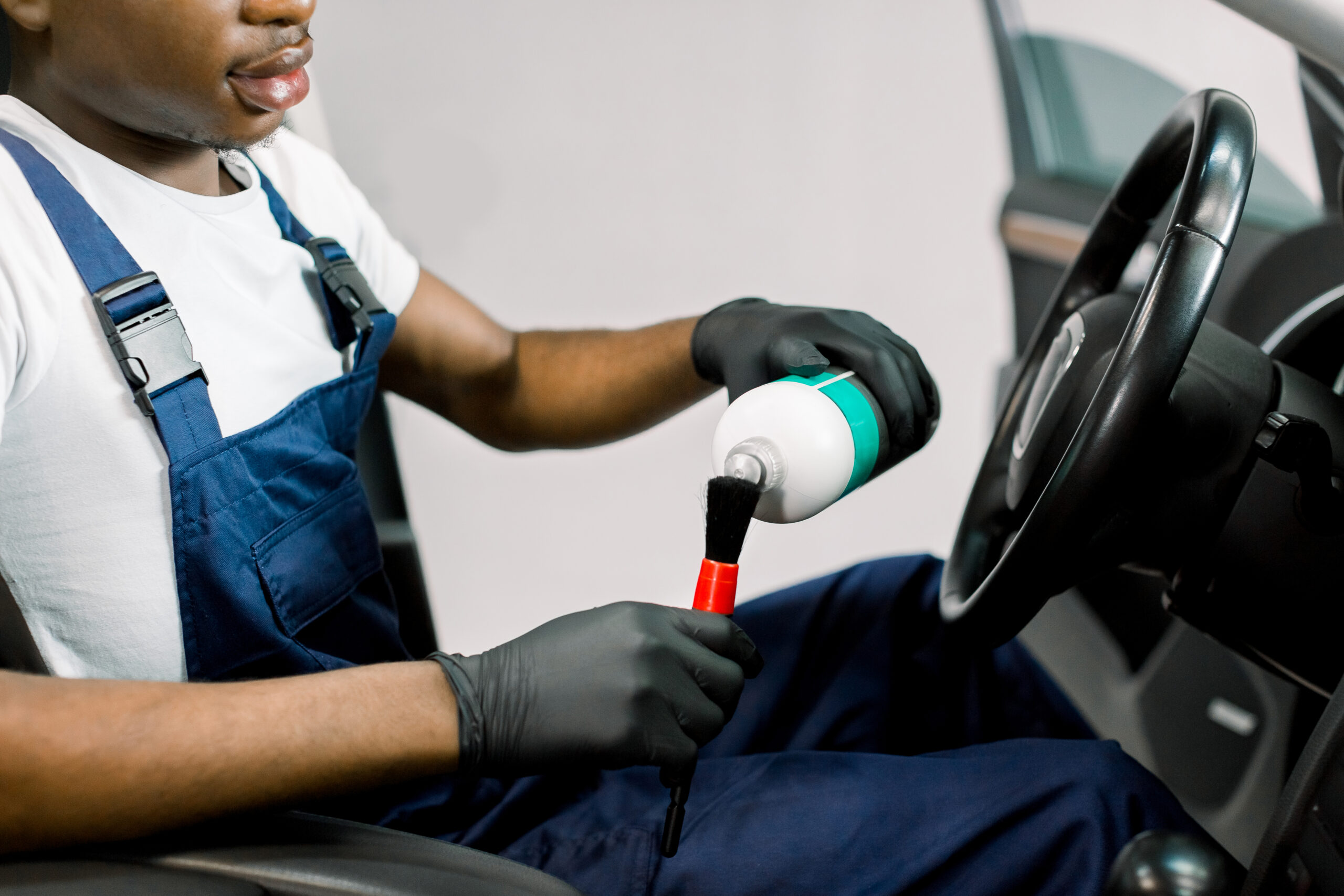 A close-up of a young African man's hands, wearing black nitrile gloves, meticulously applying car wax to a vehicle's exterior with a microfiber cloth.