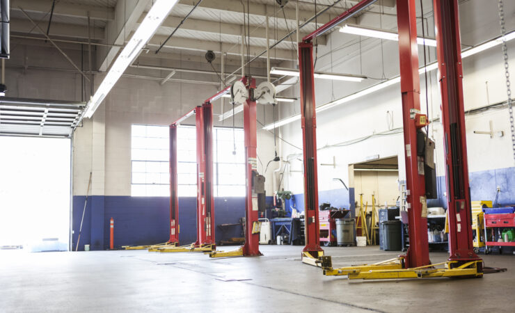 A spacious, well-lit auto repair shop with empty work bays, neatly organized tools on pegboards, and a vehicle lift in the center.