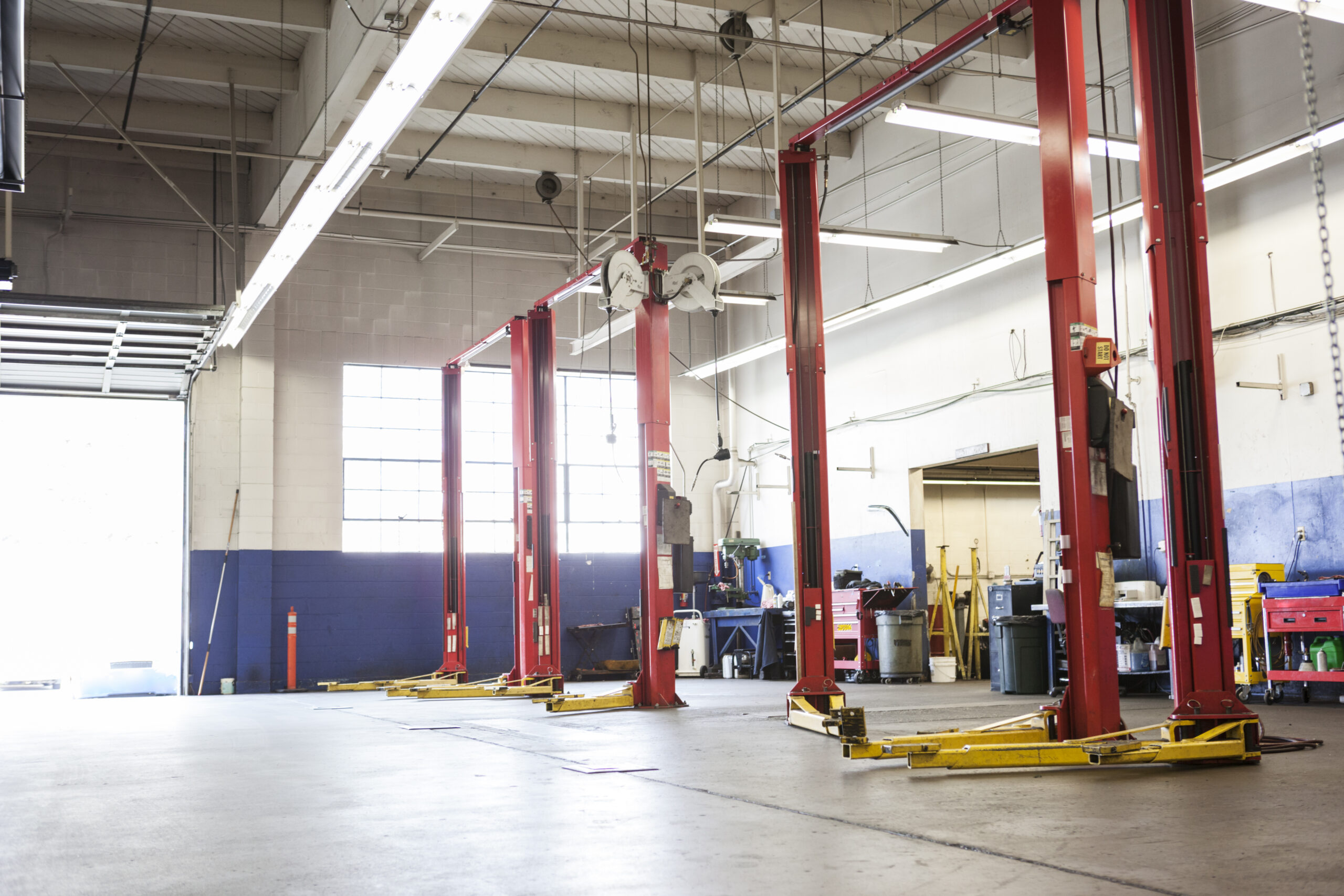 A spacious, well-lit auto repair shop with empty work bays, neatly organized tools on pegboards, and a vehicle lift in the center.