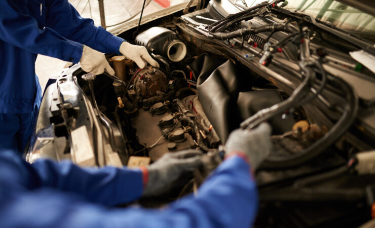 A mechanic, wearing a grease-stained uniform and safety glasses, lies on a creeper under a car, using a wrench to tighten a bolt on the engine.