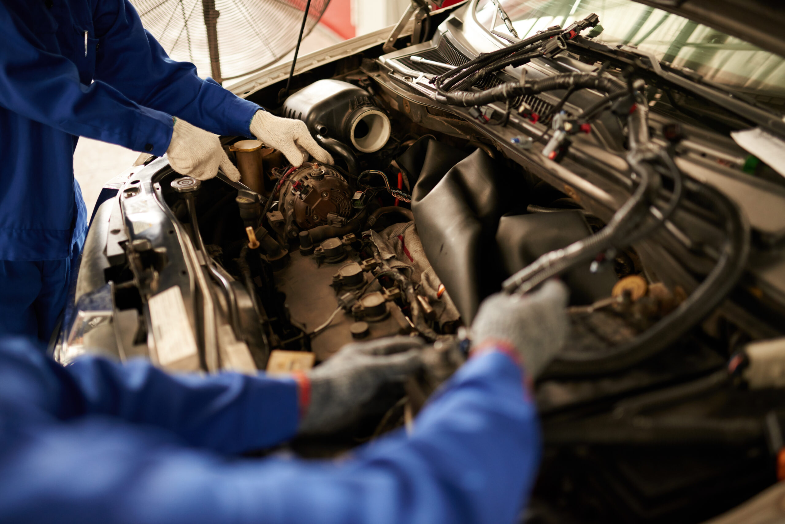 A mechanic, wearing a grease-stained uniform and safety glasses, lies on a creeper under a car, using a wrench to tighten a bolt on the engine.