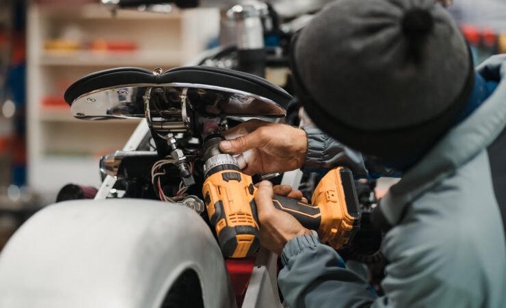 A focused mechanic, clad in a leather jacket and jeans, leans over a motorcycle in a well-lit workshop, carefully adjusting the carburetor.