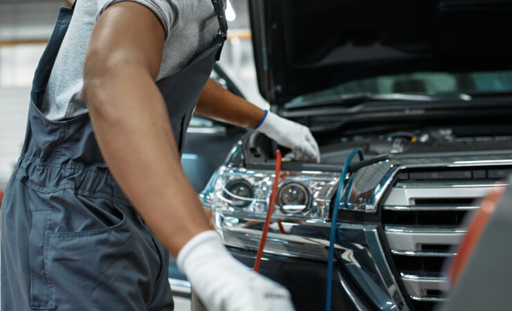 A male technician in a blue uniform carefully connects a refrigerant hose to a car's air conditioning system.