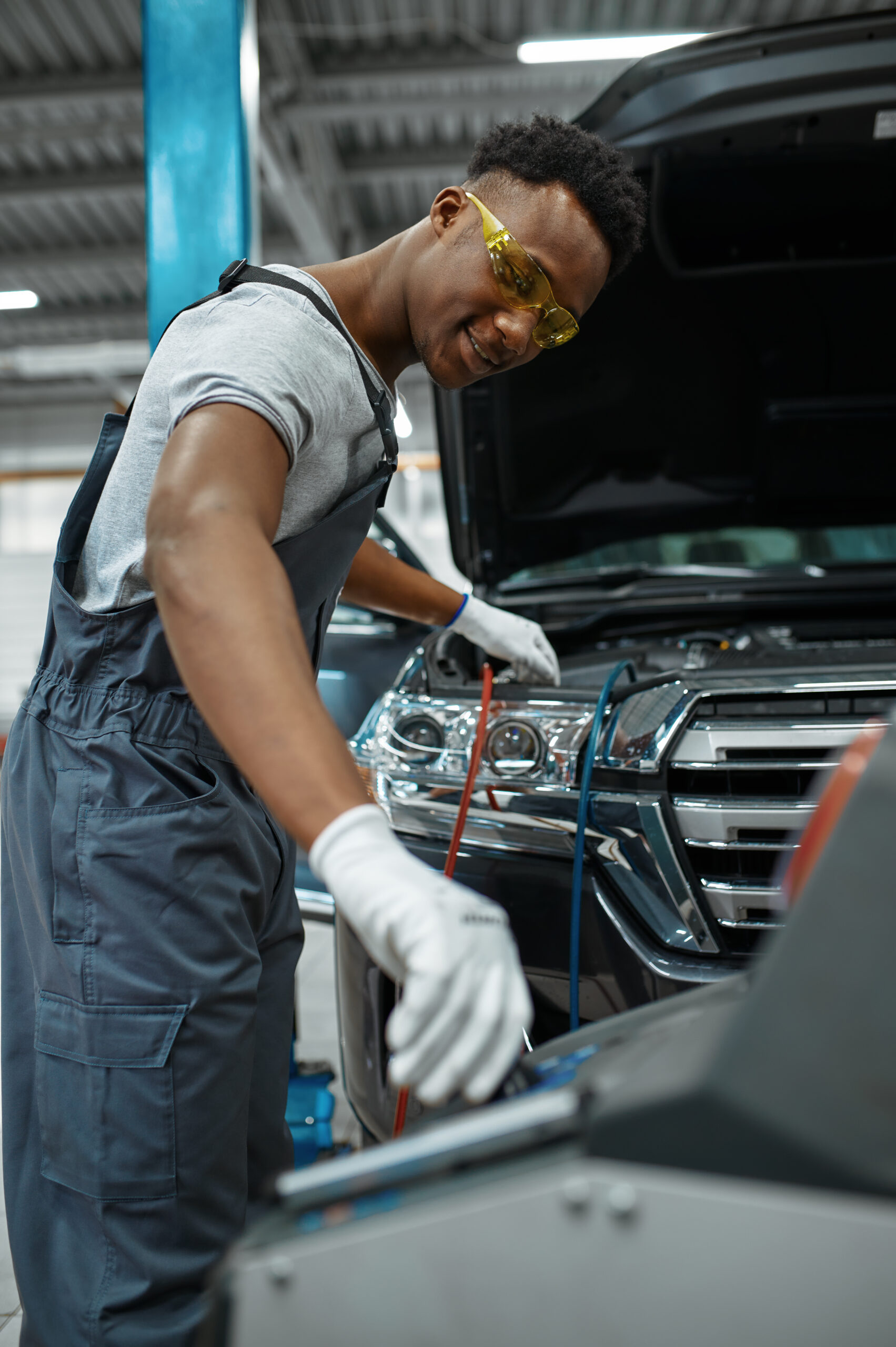 A male technician in a blue uniform carefully connects a refrigerant hose to a car's air conditioning system.