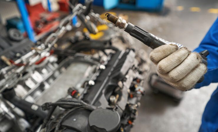 A man in a blue work shirt and gloves holds a rusty brake caliper in his hands, inspecting it closely.