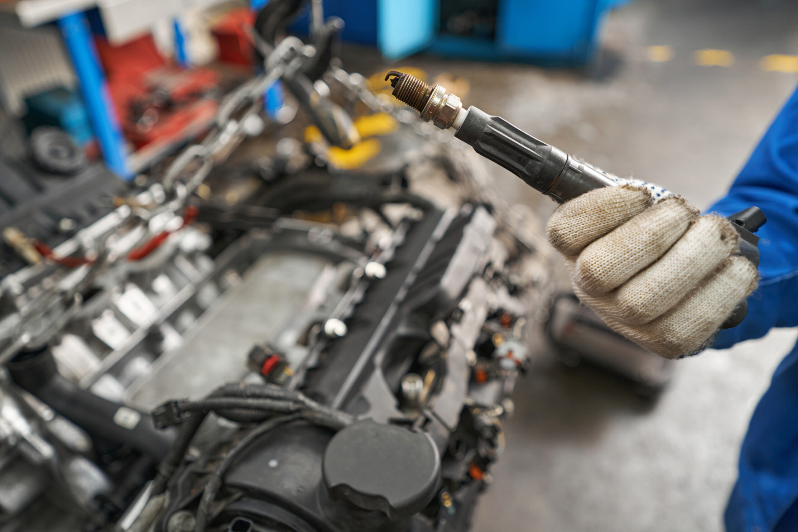 A man in a blue work shirt and gloves holds a rusty brake caliper in his hands, inspecting it closely.