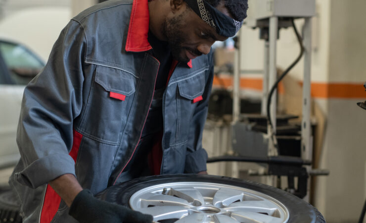 A mechanic in a blue jumpsuit carefully examines a tire's tread and sidewall, selecting the right fit for a customer's vehicle.