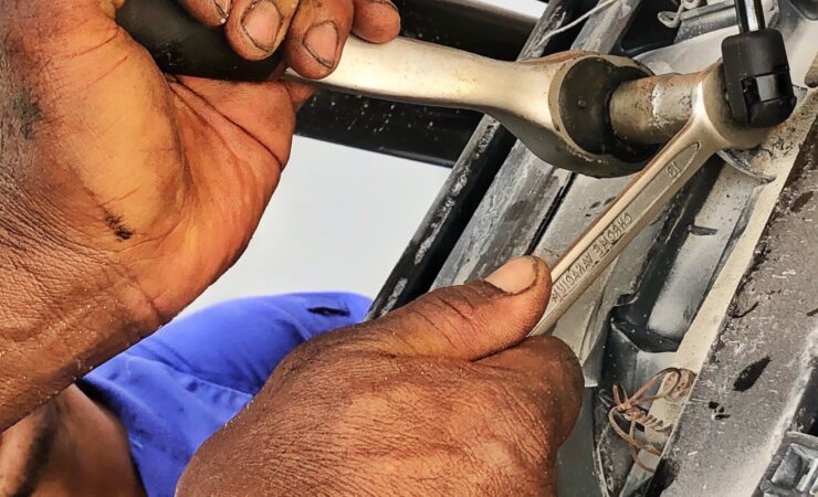 A mechanic, wearing a grease-stained uniform, lies under a car and uses a wrench to loosen a bolt.