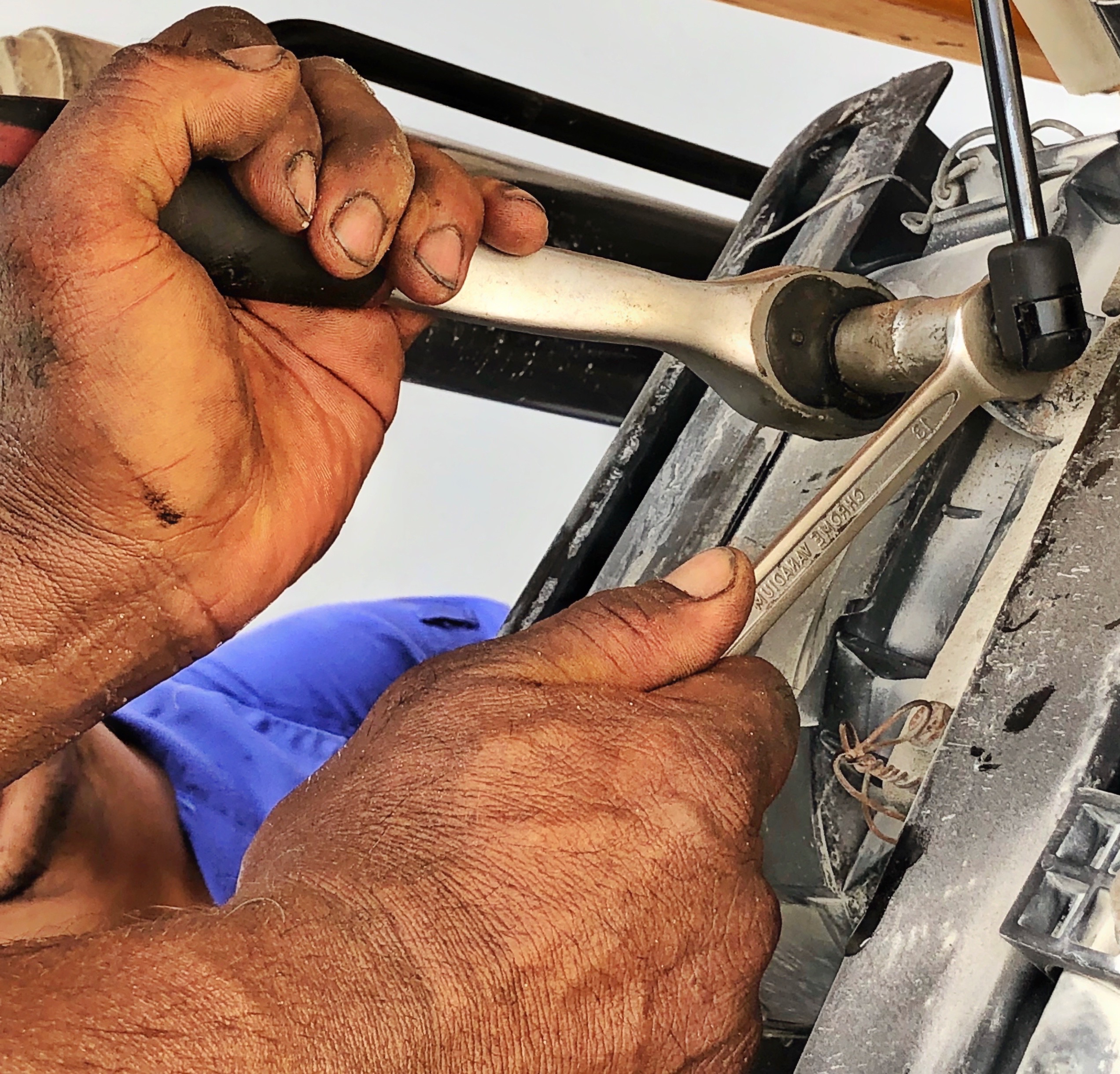 A mechanic, wearing a grease-stained uniform, lies under a car and uses a wrench to loosen a bolt.