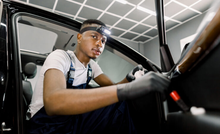 A young African man, wearing a hard hat and safety vest, smiles confidently while holding a toolbox.