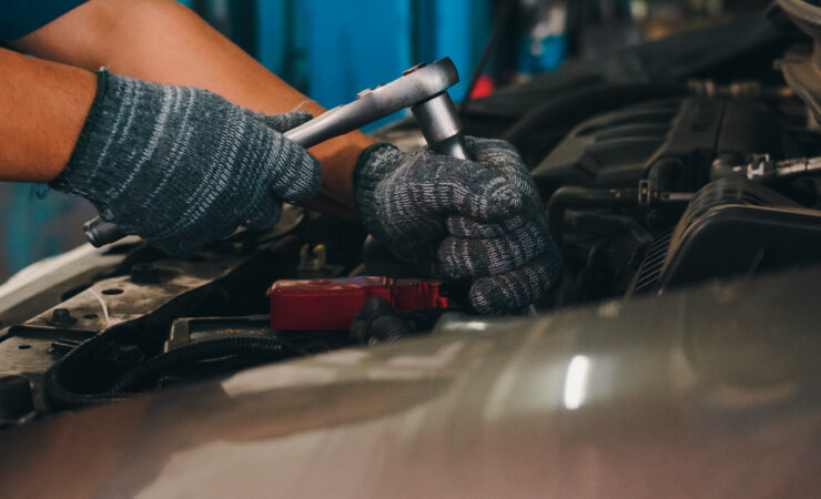 A professional car mechanic, using a socket wrench, carefully tightens a bolt on a car engine raised on a lift.