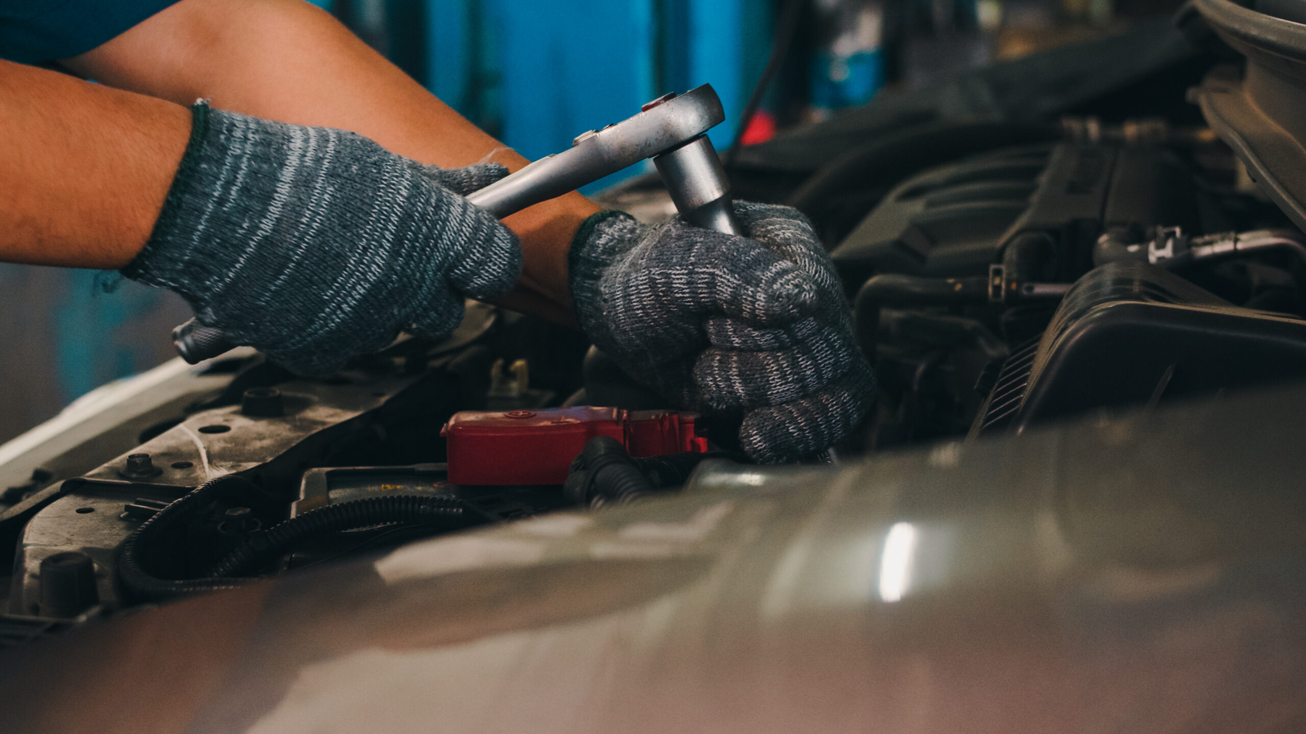 A professional car mechanic, using a socket wrench, carefully tightens a bolt on a car engine raised on a lift.