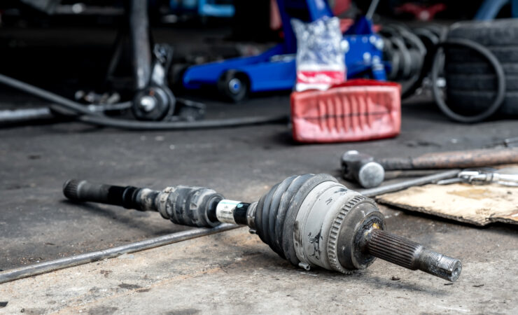 A mechanic, lying on their back under a car, replaces a worn-out universal joint on a drive shaft.