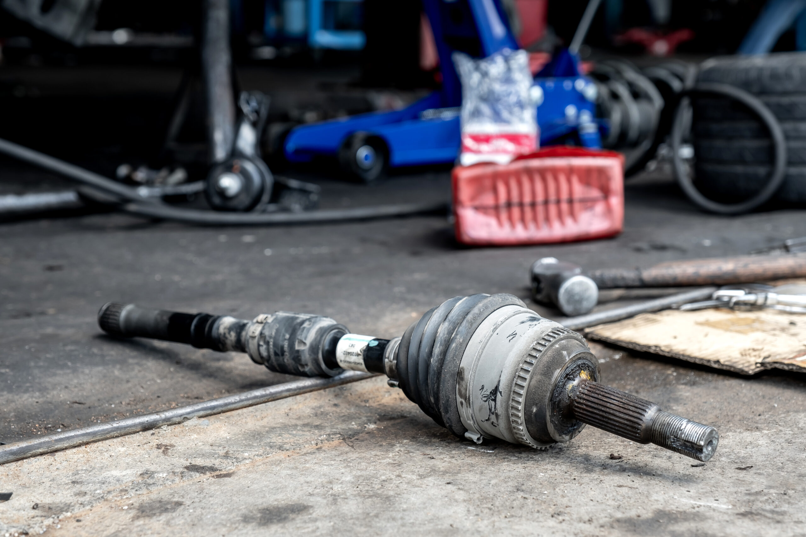 A mechanic, lying on their back under a car, replaces a worn-out universal joint on a drive shaft.