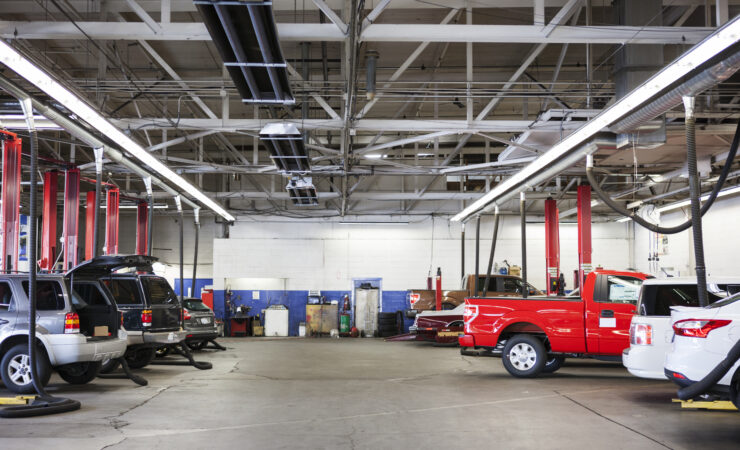 A bustling auto repair shop with rows of cars and trucks in various stages of repair, mechanics working diligently underneath and around them