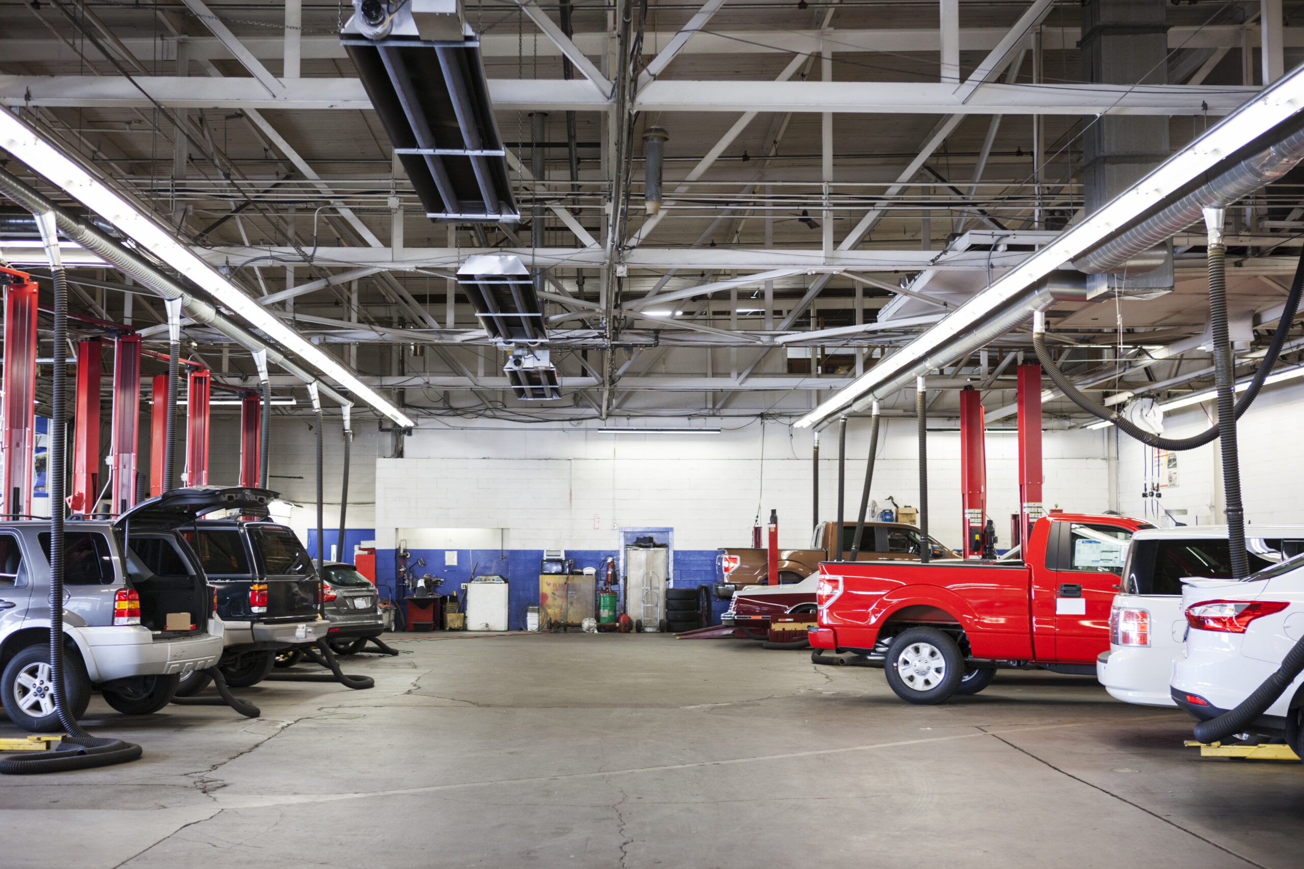 A bustling auto repair shop with rows of cars and trucks in various stages of repair, mechanics working diligently underneath and around them