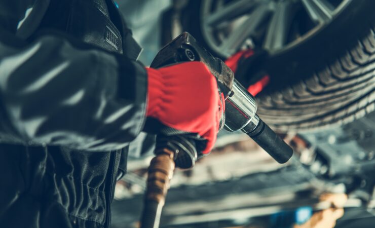 A mechanic in a garage uses a power wrench to remove lug nuts from a car's wheel, preparing to swap out seasonal tires.