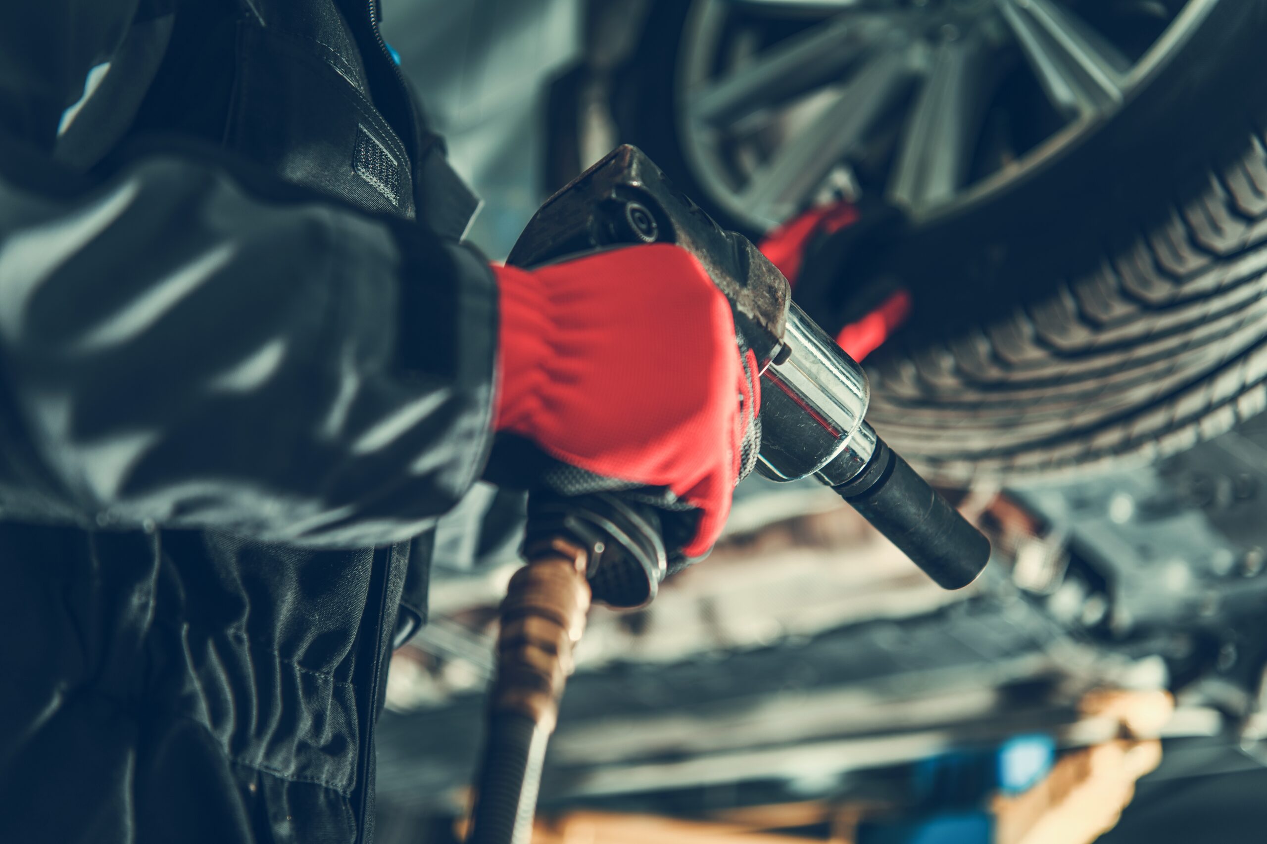 A mechanic in a garage uses a power wrench to remove lug nuts from a car's wheel, preparing to swap out seasonal tires.