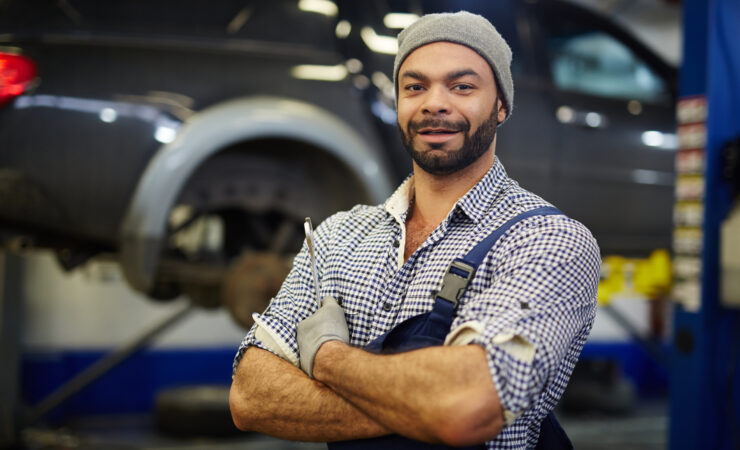 An upkeep worker in a blue uniform and hard hat, holding a wrench, smiles while standing in front of a large industrial machine.