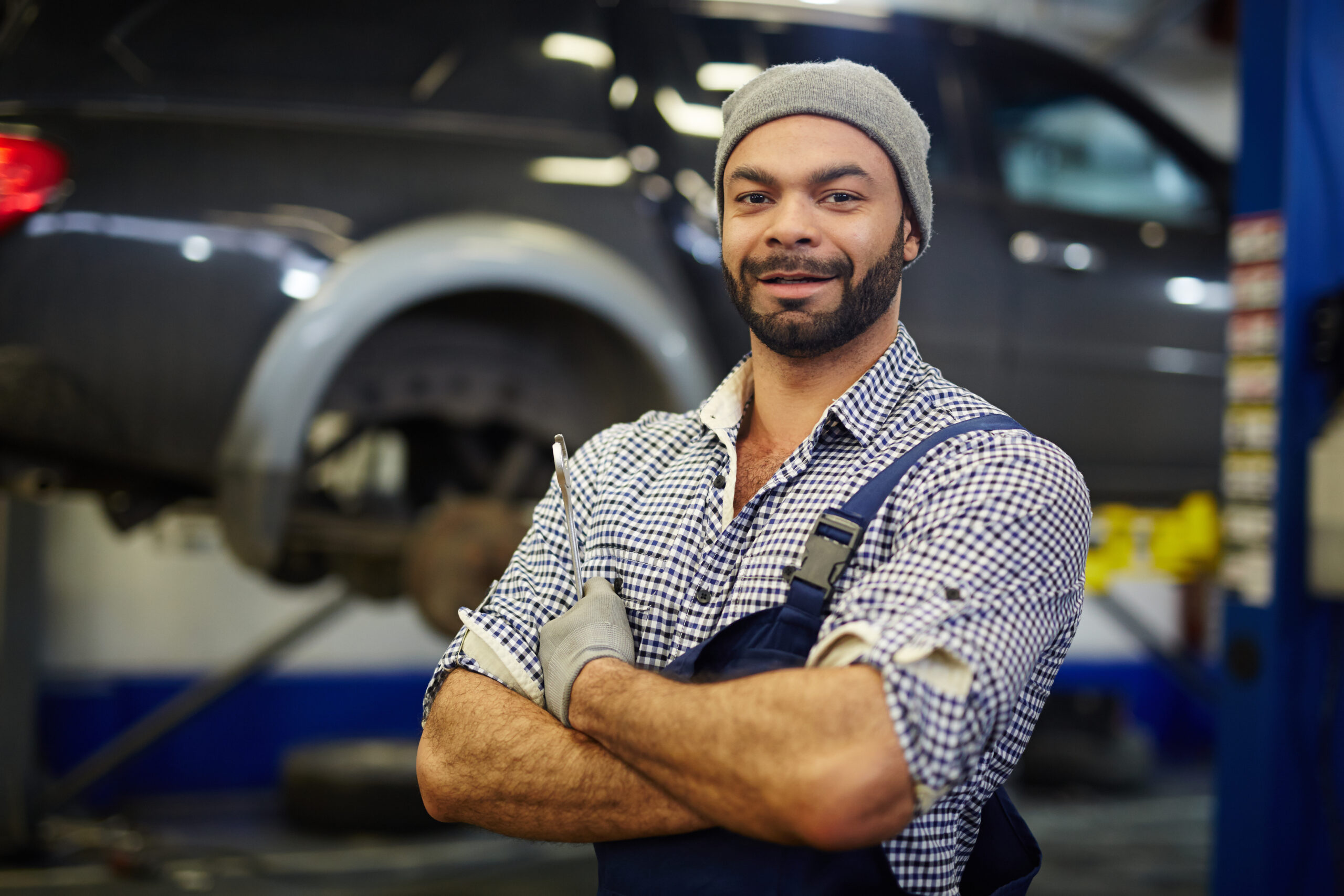 An upkeep worker in a blue uniform and hard hat, holding a wrench, smiles while standing in front of a large industrial machine.