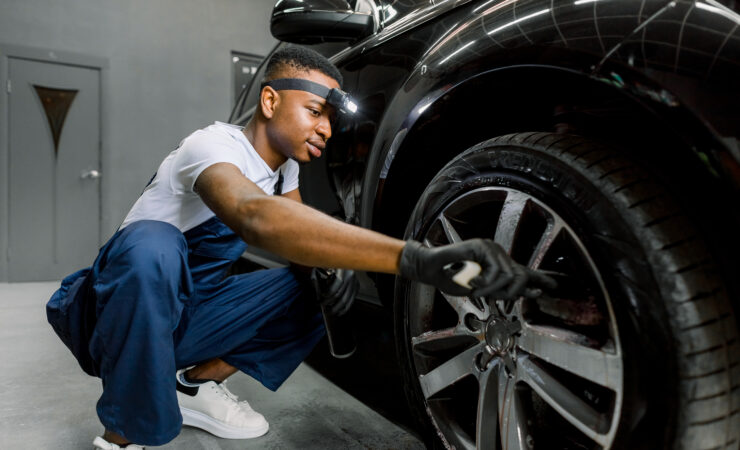 A person wearing a blue t-shirt and jeans meticulously hand washes a white car using a sponge and soapy water.