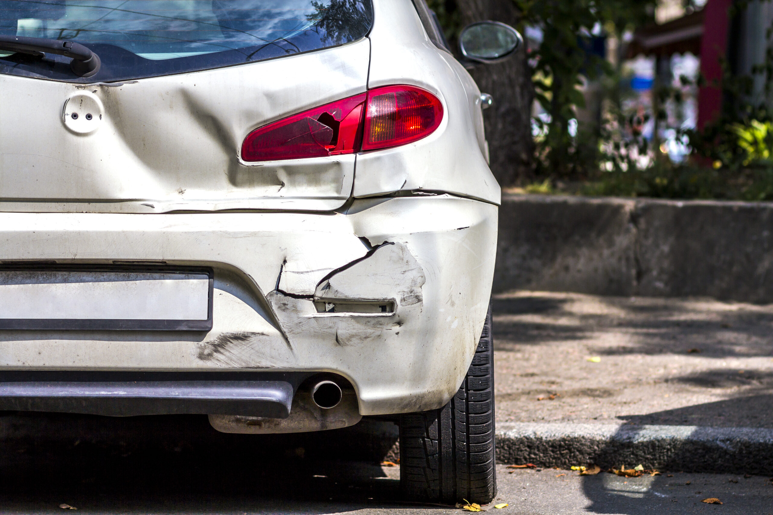 A white car with extensive damage to the rear bumper and trunk after a collision.