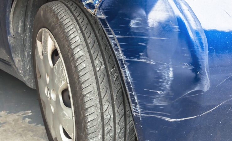 A close-up of a car with a large dent and multiple scratches on its side panel.