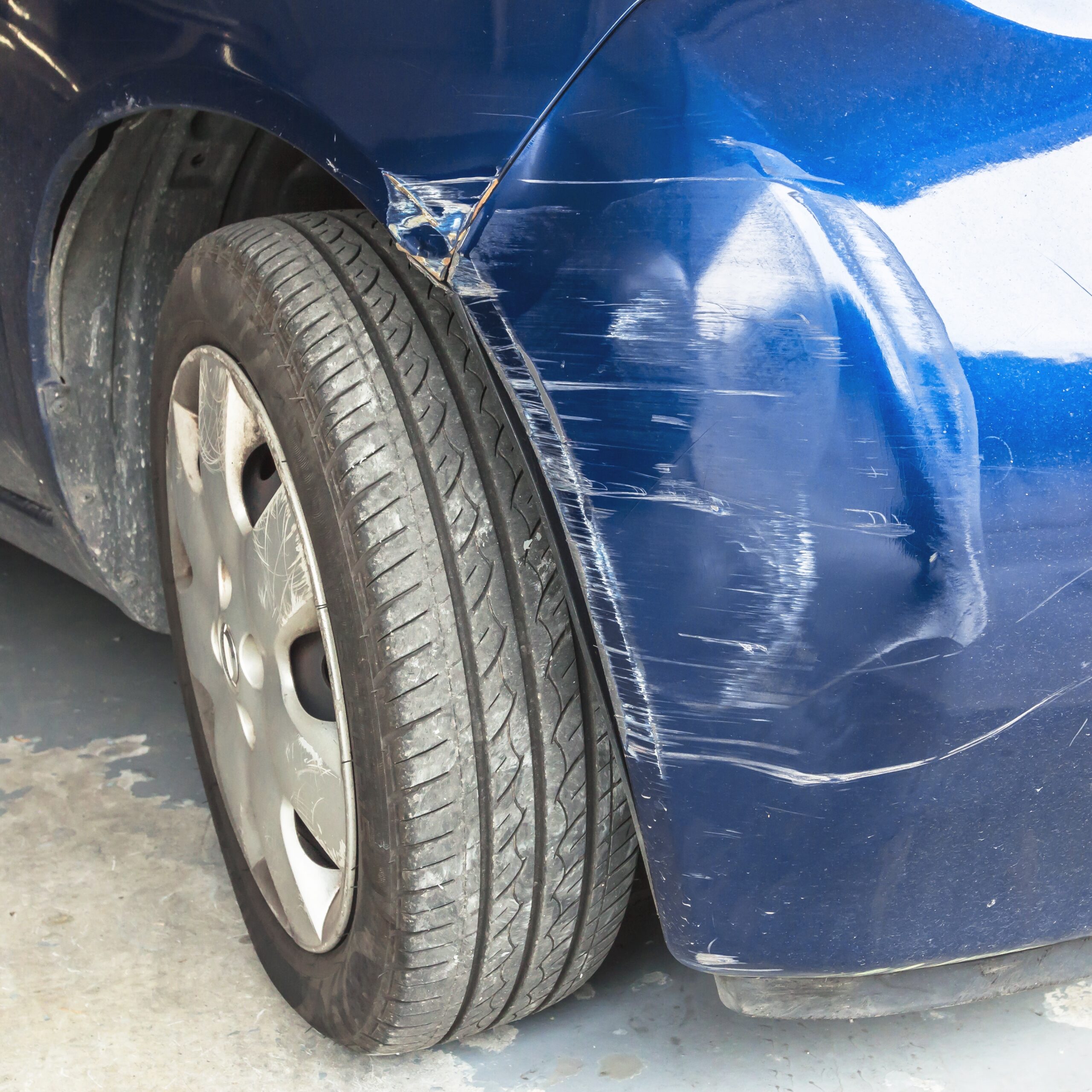 A close-up of a car with a large dent and multiple scratches on its side panel.