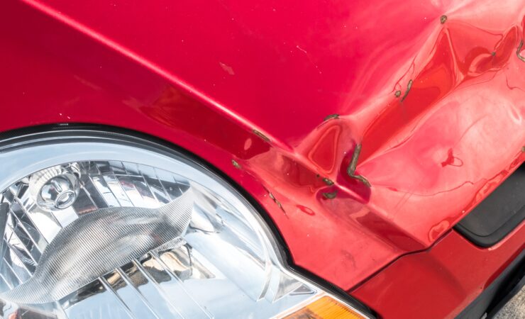 A red car with significant damage to its front end, including a crumpled hood and shattered headlights.