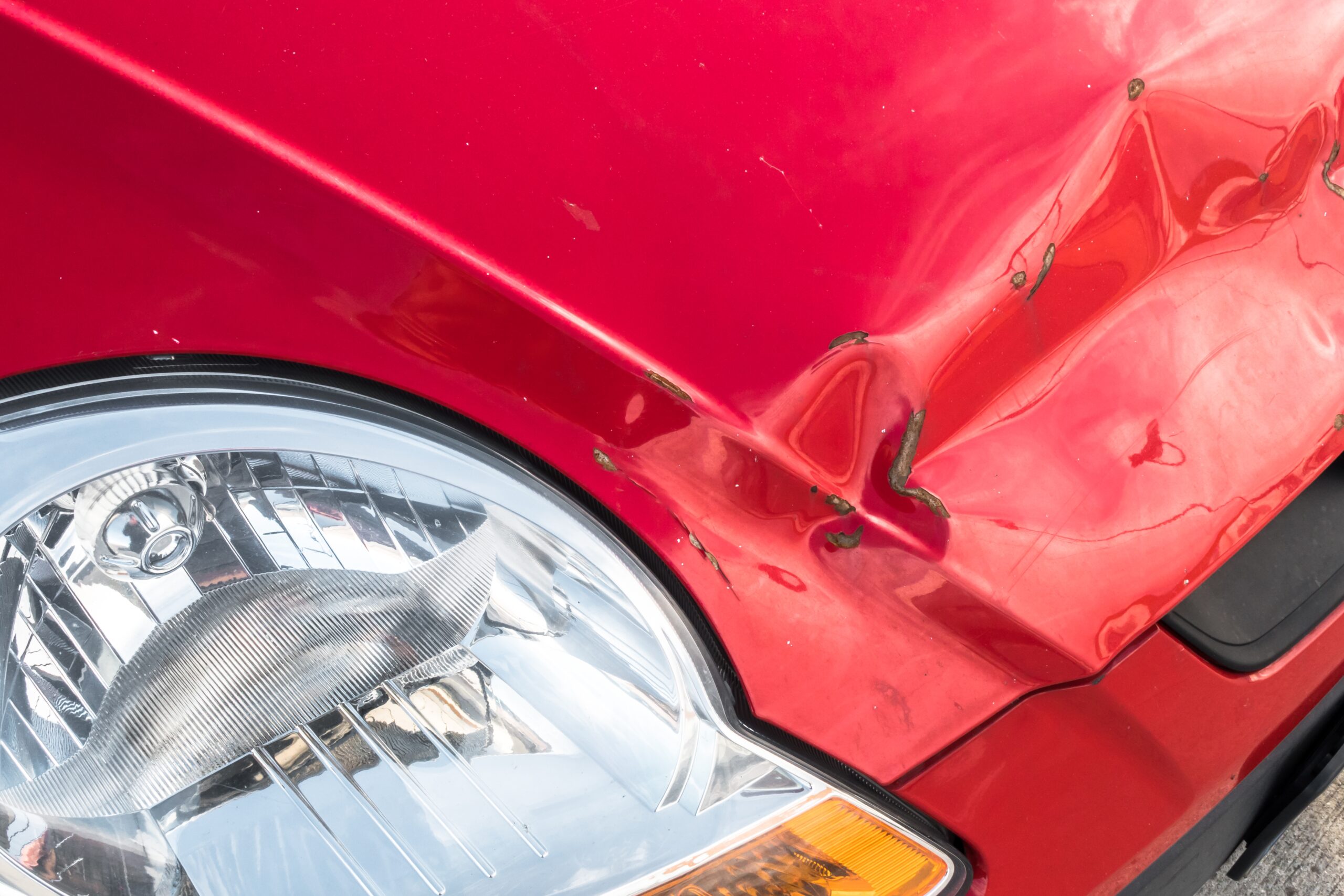 A red car with significant damage to its front end, including a crumpled hood and shattered headlights.