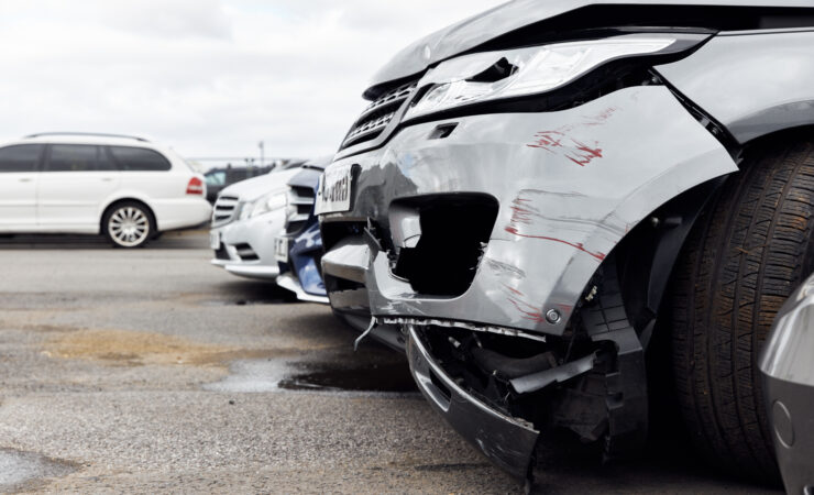 A car with smashed windows, graffiti, and dents parked in a car park.