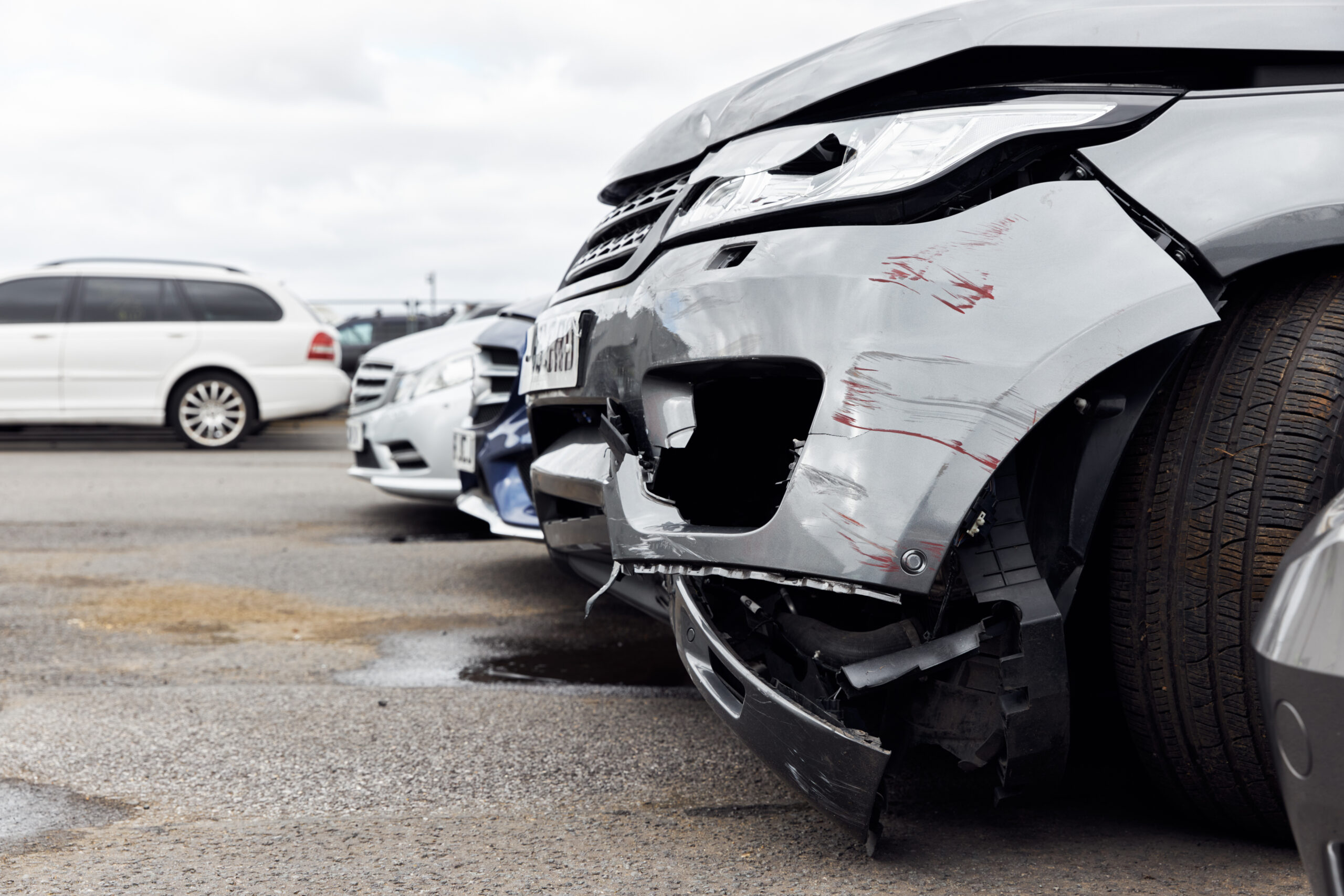 A car with smashed windows, graffiti, and dents parked in a car park.